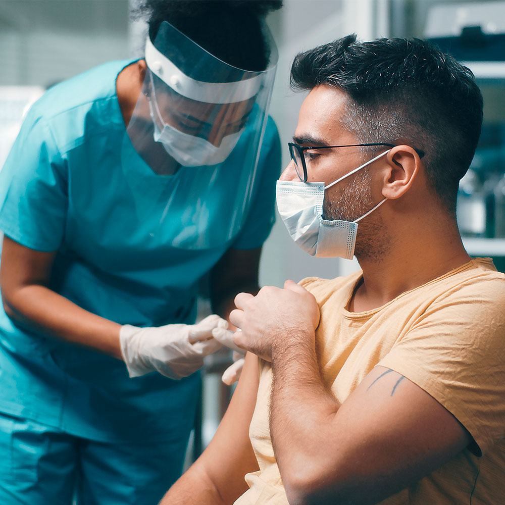 Woman in scrubs and face shield delivers vaccination to man in face mask